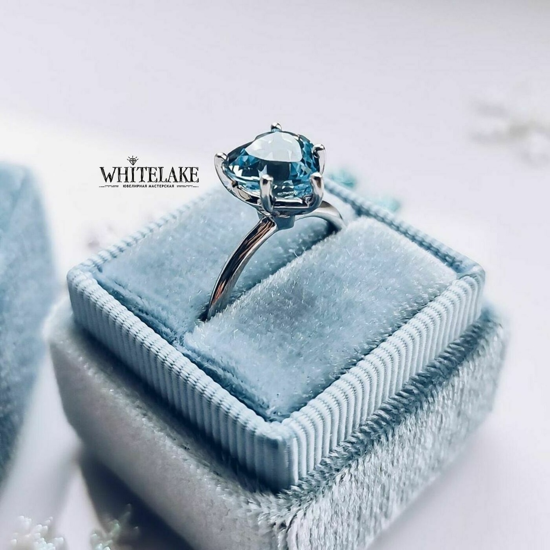 Уникальное кольцо с камнем сердечком из белого золота, украшенное топазом Swiss, лежащее в бархатной голубой коробочке